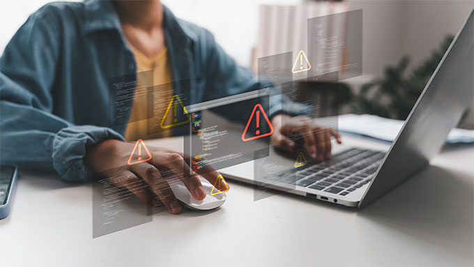 Person using a laptop with overlaid code and warning icons.